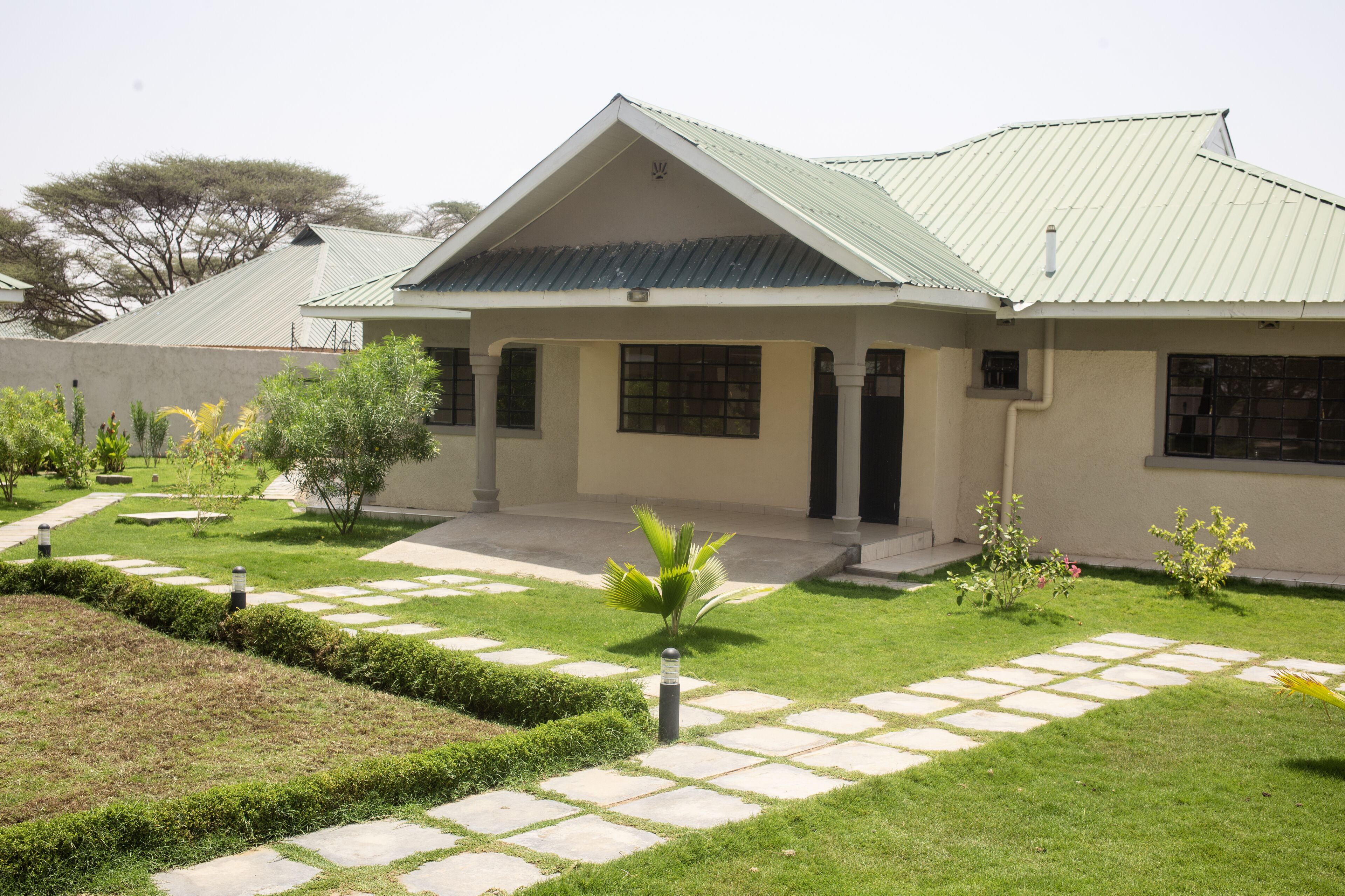 Une maison à deux étages avec un toit végétalisé, une allée pavée et un jardin bien entretenu, agrémenté de diverses plantes et d’un sentier.