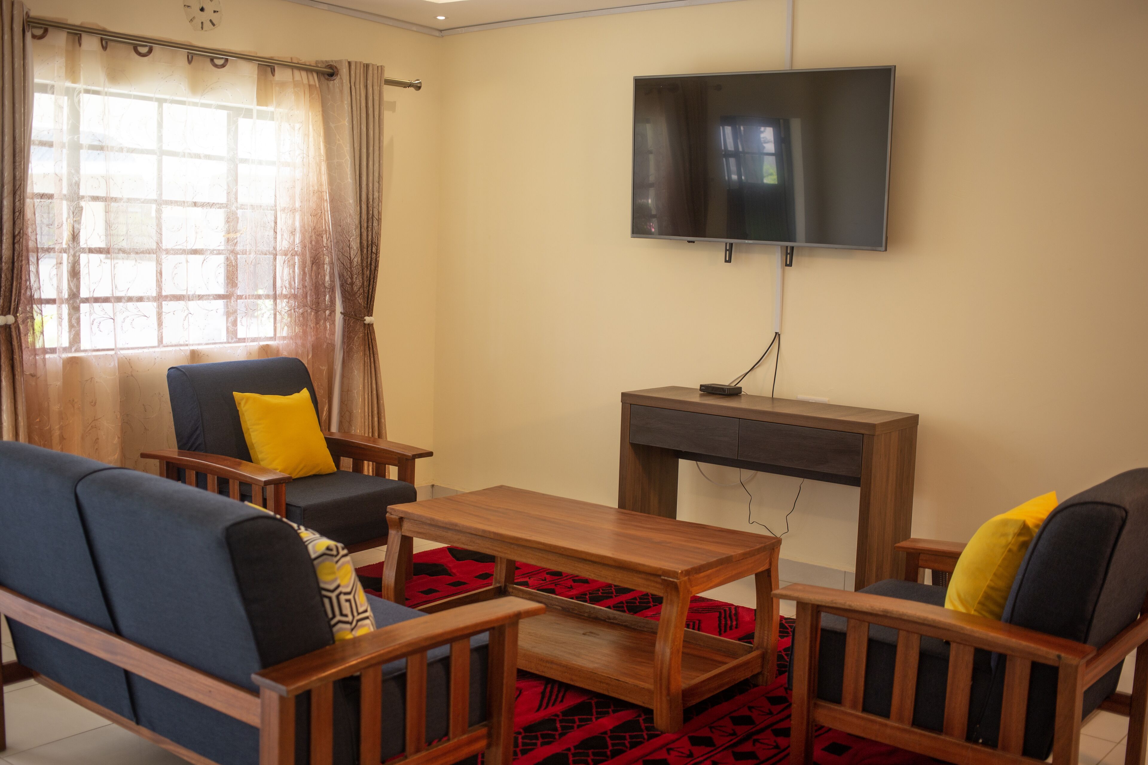 Una sala de estar con televisor, muebles de madera y un tapete rojo estampado.