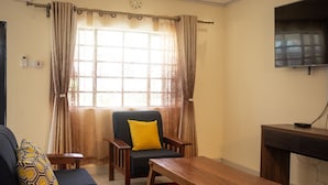 A living room with a sofa, armchair, wooden coffee table, and a TV mounted on the wall. - Cairo Palace Hotel (Lodwar)