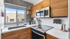 Une cuisine moderne avec des meubles en bois, un four à micro-ondes en acier inoxydable, une cuisinière à gaz et une fenêtre donnant sur un bâtiment en briques.