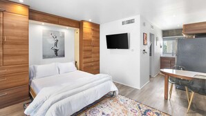 Une chambre moderne équipée d’un lit, d’une télévision, d’armoires en bois et d’un petit coin cuisine.