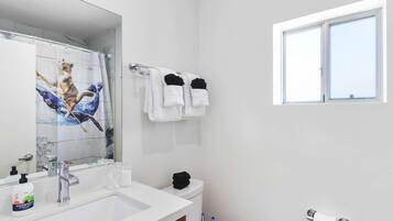A modern bathroom with a large mirror, white sink, and a toilet. There is a window providing natural light and a towel rack with white towels.