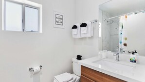 A modern bathroom with a white sink, a large mirror, a toilet, and a towel rack with towels. - Poolside Studio in Central DTPH Location w/ Pool (Phoenix)