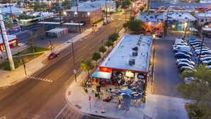 A street-level view of a building with a covered outdoor seating area, a mural, and a parking lot. - Poolside Studio in Central DTPH Location w/ Pool (Phoenix)