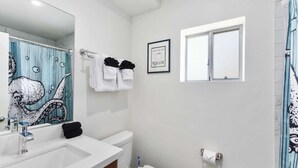 Een badkamer met een witte wasbak, toilet en een douchegordijn met een blauw-wit patroon, en een ingelijst schilderij aan de muur.
