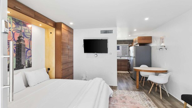 Een moderne hotelkamer met een groot bed, een flatscreen televisie, een zithoek met tafel en stoelen, en een keuken op de achtergrond.