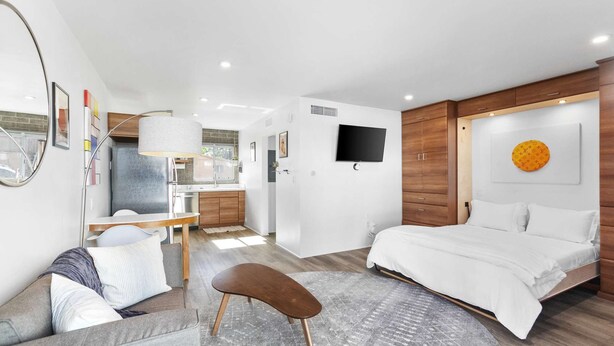 A modern hotel room with a bed, a desk, a chair, a TV, and a bathroom. - DTPH Mid Century Studio w/Pool & Parking (Phoenix)