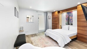 A modern bedroom with a bed, a wooden wardrobe, a mirror, and a cityscape artwork on the wall. - DTPH Mid Century Studio w/Pool & Parking (Phoenix)