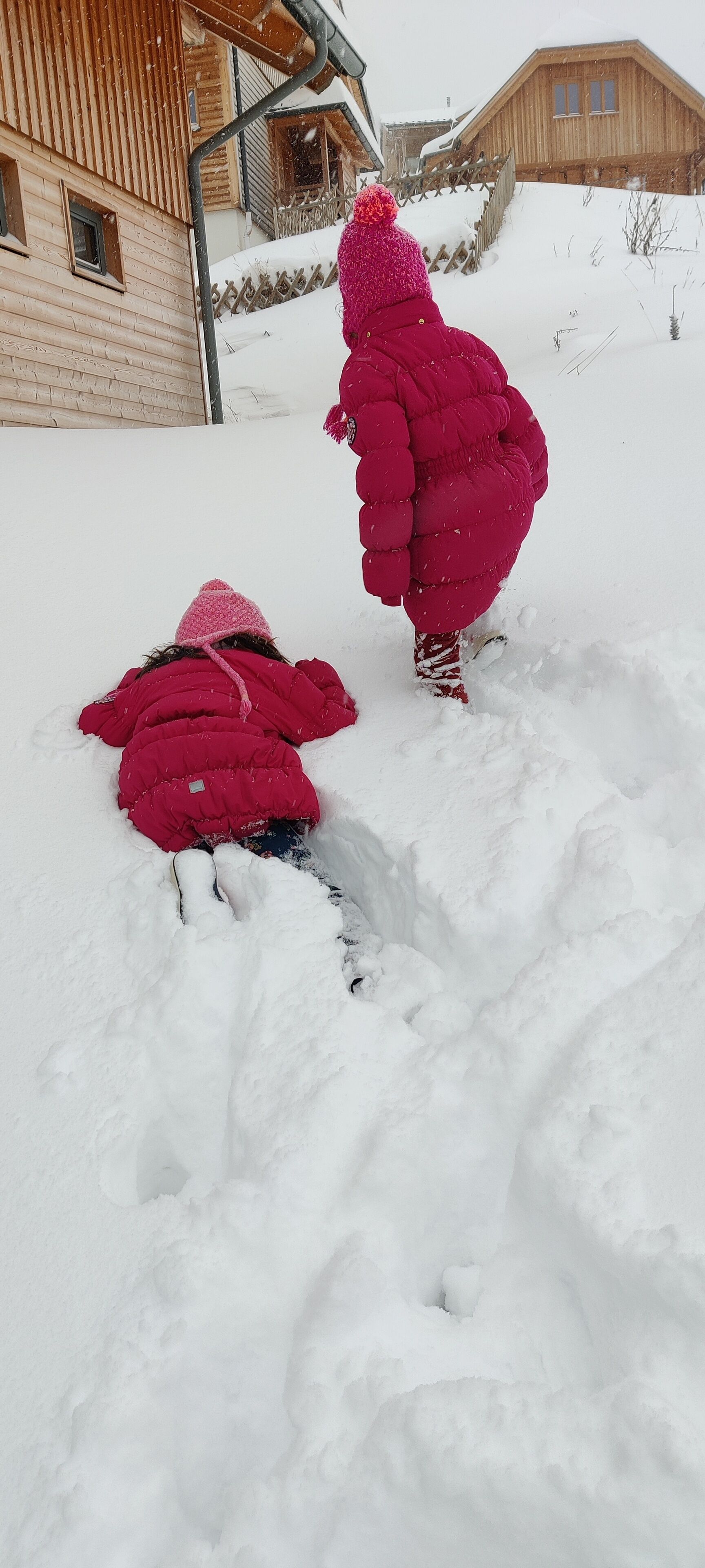 Two children playing in a snowy outdoor area with wooden buildings in the background.