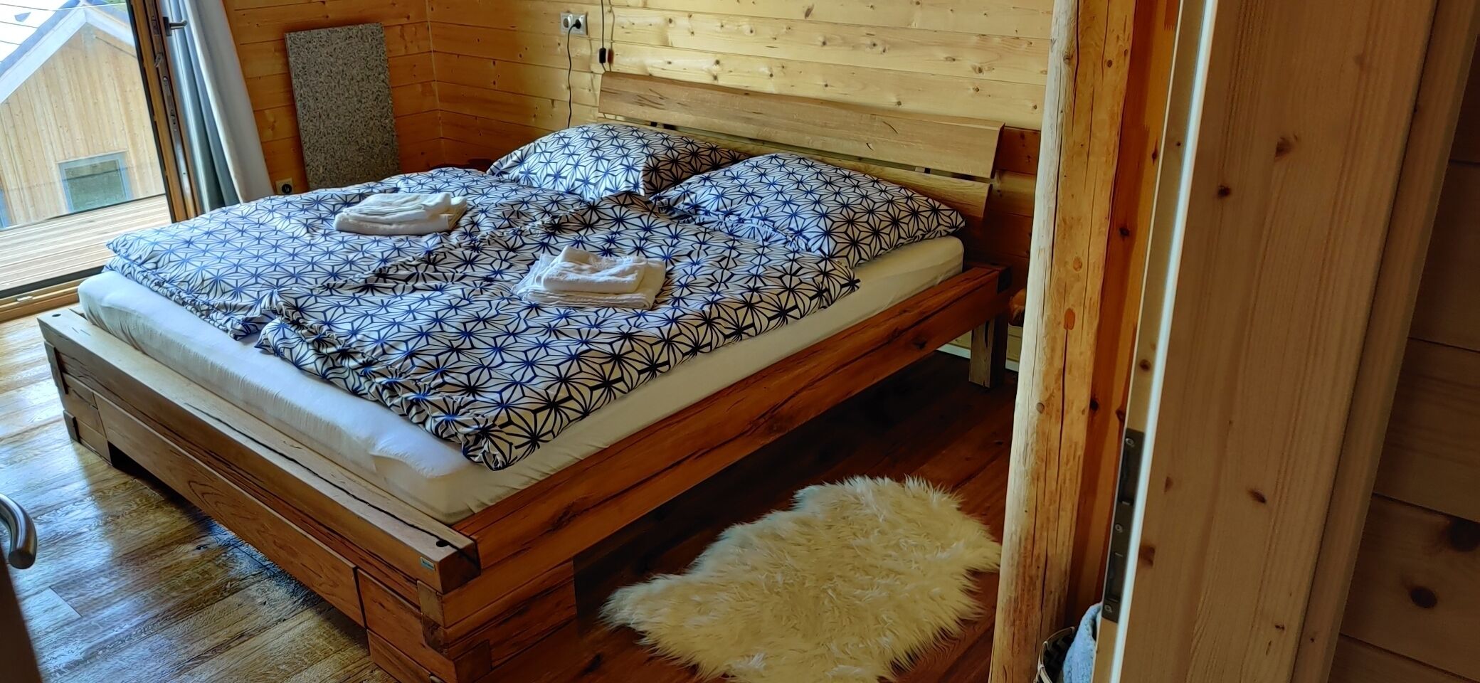 A wooden bed with a geometric patterned bedspread and pillows, a fluffy white rug, and a wooden headboard.