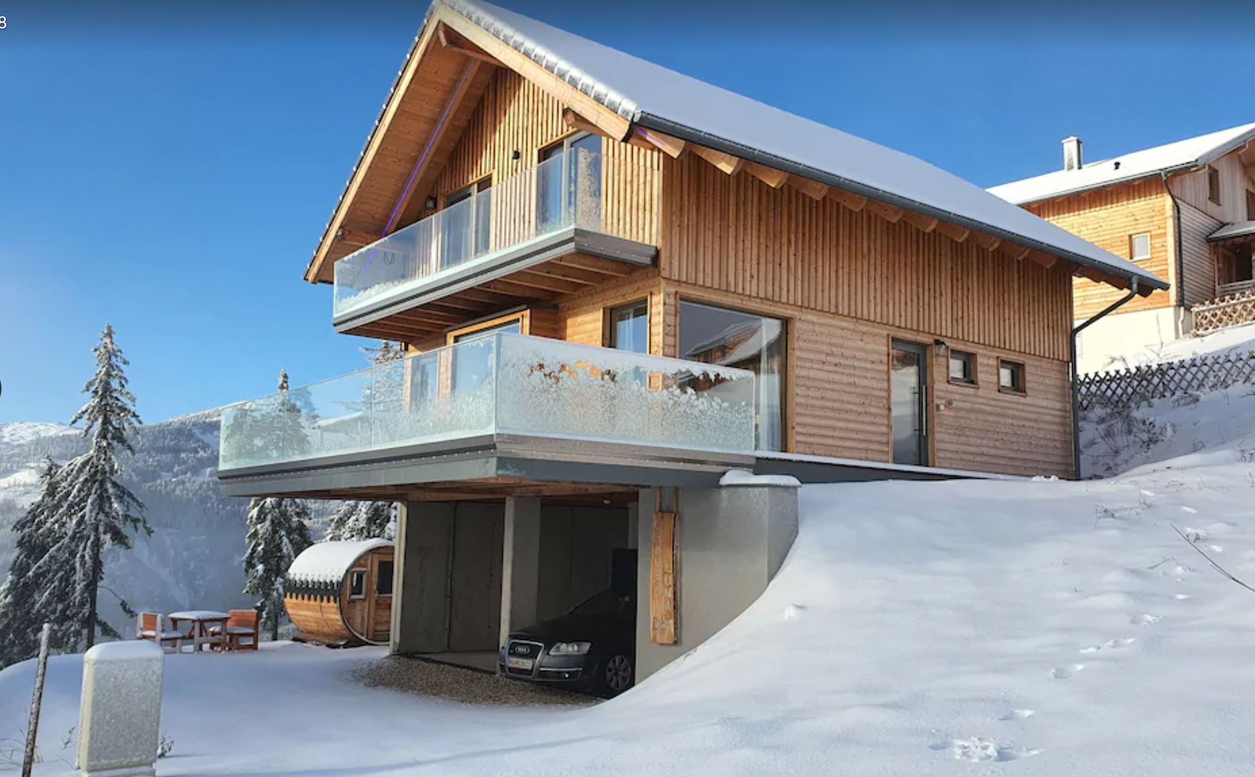 Un moderno chalet de madera con balcón, entrada cubierta y un telesilla al fondo.