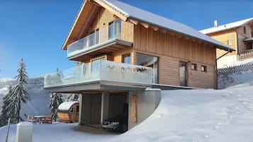 Un moderno chalet de madera con balcón, entrada cubierta y un telesilla al fondo.