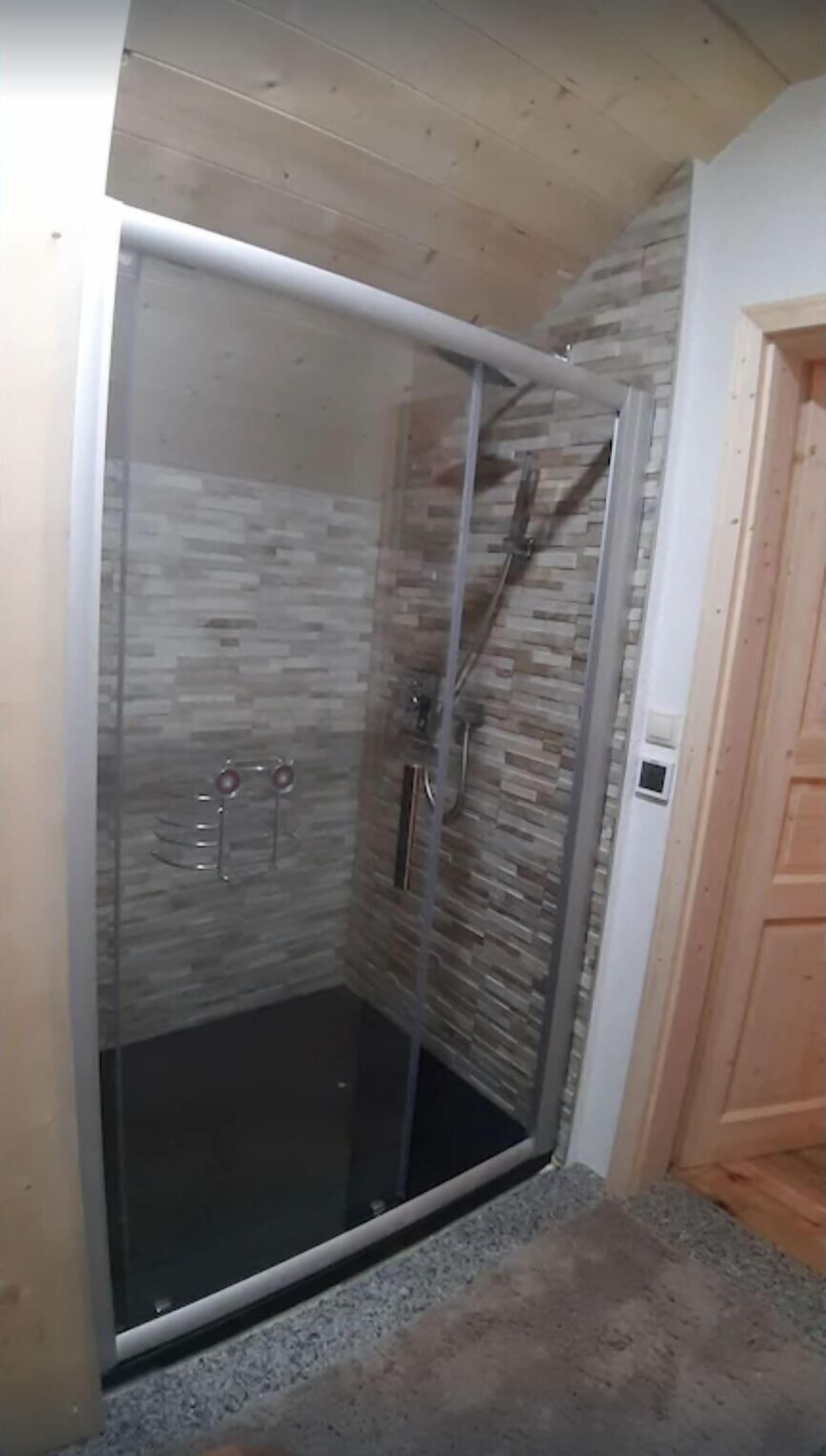 Un área de ducha con paredes de piedra y techo de madera, todo ello envuelto en vidrio.