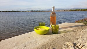 Eine Weinflasche, eine grüne Schale und ein grünes Glas auf einer Betonstufe an einem Gewässer.