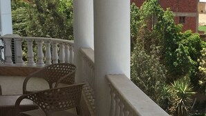 Un balcone con ringhiera bianca, una sedia in vimini e un tavolino.