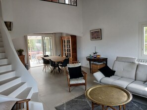 Amplia sala de estar con una escalera, una mesa de comedor, un sofá y vistas a través de un ventanal abierto.
