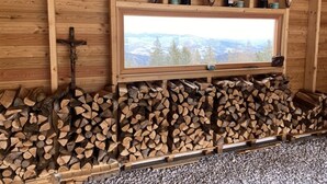 A rustic wooden interior with a window overlooking a snowy landscape, wooden shelves with wine bottles and antlers, and neatly stacked firewood. - Klippitztörl - The exclusive chalet for discerning nature lovers (Bad St. Leonhard)