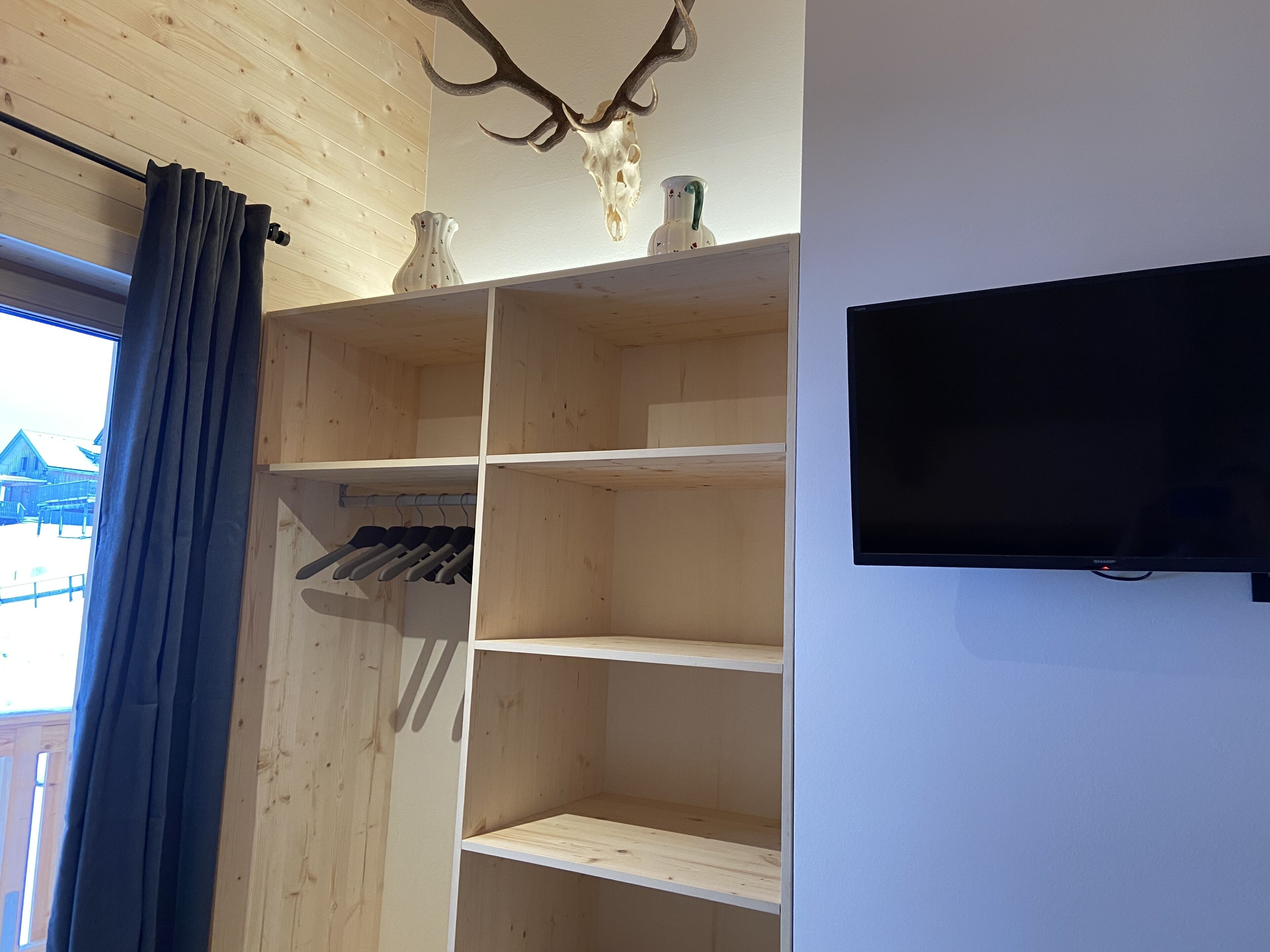 Een kamer met een houten kledingkast, een wandtelevisie en een raam met gordijnen.