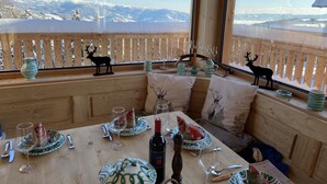 A wooden cabin with a dining area featuring a table set for two, a view of snow-covered mountains, and a wooden railing with reindeer decorations. - Klippitztörl - The exclusive chalet for discerning nature lovers (Bad St. Leonhard)