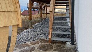 A wooden deck with a staircase leading to a balcony, surrounded by stone tiles and a white wall. - Klippitztörl - The exclusive chalet for discerning nature lovers (Bad St. Leonhard)