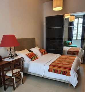 A hotel room with a bed, a desk, a chair, a lamp, and a large mirror.