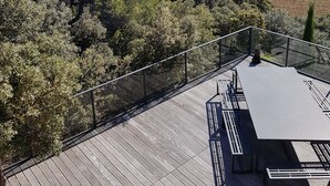 Een houten terras met een tafel en banken, uitkijkend op een vallei met bomen en een berg in de verte.