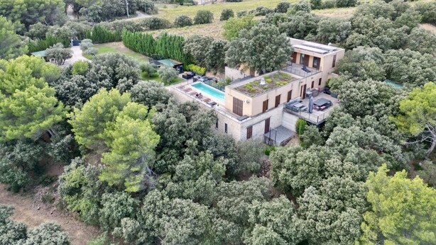 Een moderne villa met een zwembad op het dak, omringd door weelderige begroeiing en heuvels op de achtergrond.