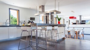 Een moderne keuken met een centraal eiland, barkrukken en een eethoek met een tafel en stoelen.