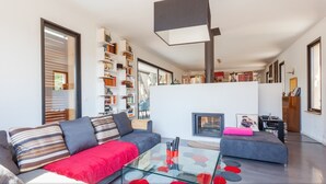 Een moderne woonkamer met een glazen salontafel, een bank met gestreepte kussens, een open haard en een boekenplank vol boeken.