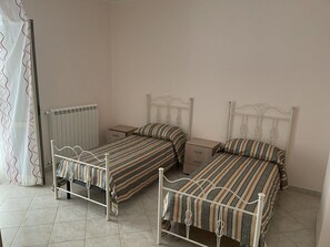Two single beds with metal frames and striped bedding, accompanied by bedside tables and a wavy-patterned curtain.