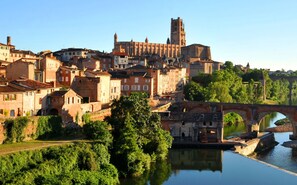 A historic town with a prominent church and a bridge over a river. - Le Domaine de la Monestarié<br>Charm, elegance and scents of Tuscany (BERNAC, TARN)