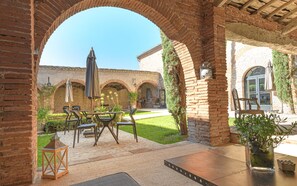 An outdoor patio area with brick arches, a table with chairs, and potted plants. - Le Domaine de la Monestarié<br>Charm, elegance and scents of Tuscany (BERNAC, TARN)