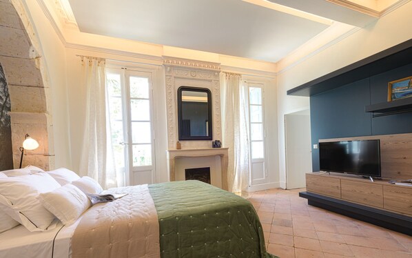 A bedroom with a bed, a fireplace, a TV, and a stone wall. - Le Domaine de la Monestarié<br>Charm, elegance and scents of Tuscany (BERNAC, TARN)