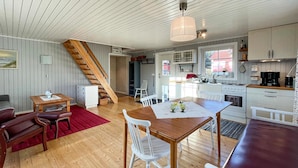 Een gezellige, goed verlichte kamer met een houten eettafel, witte stoelen, een rood tapijt en een houten trap die naar een andere kamer leidt.