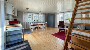 Een ruime kamer met houten vloer, een zithoek met tafel en stoelen, een rood vloerkleed en een houten trap.