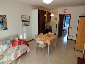Ein gemütliches Wohnzimmer mit einer Couch, einem Esstisch mit Stühlen, einer Küchenzeile mit Schränken und einem Flur, der in ein weiteres Zimmer führt.