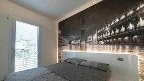 Ein Schlafzimmer mit einem großen Bett, einem Fenster mit Jalousien und einem Wandbild einer Stadtansicht.
