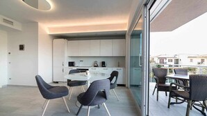 Eine moderne Wohnung mit Balkon, Essbereich mit Stühlen, Küche mit weißen Schränken und Blick auf Gebäude.