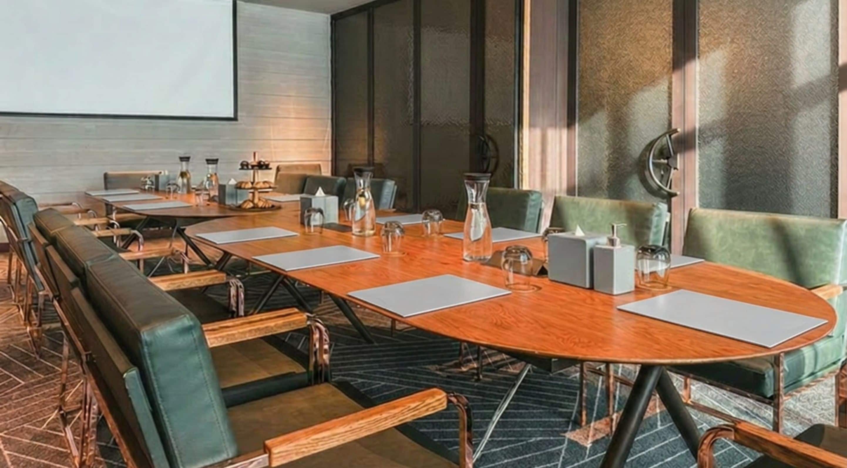 A conference room with a long table, chairs, and a projector screen.