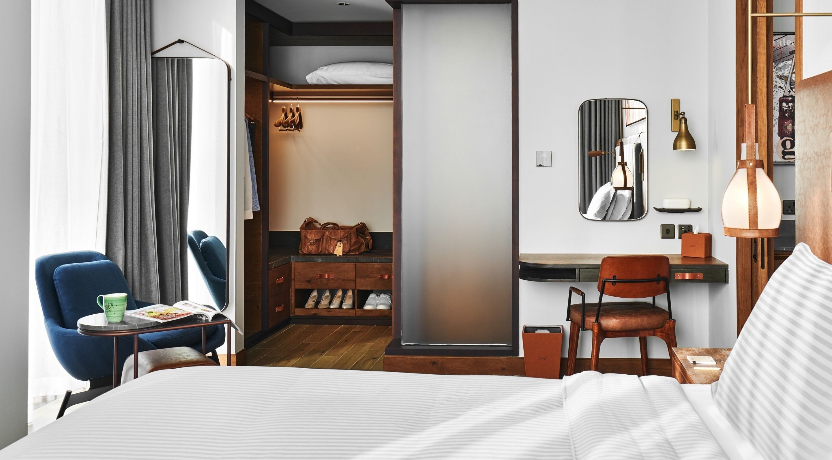 A hotel room with a bed, a desk, a chair, a wardrobe, and a mirror.