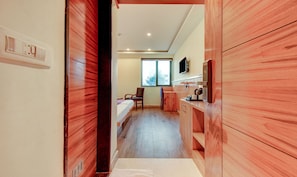 A hotel room with a wooden floor, a bed, a chair, a desk, and a window with a view of the city. - Treebo Tryst La Prosperite (Bengaluru)