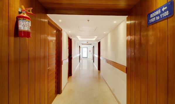 A hotel hallway with wooden paneling, a fire exit sign, and a directional sign for rooms 1101 to 1108. - Treebo Tryst La Prosperite (Bengaluru)
