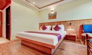 A hotel room with a large bed, wooden headboard, a nightstand with a lamp, a desk with a chair, and a painting on the wall. - Treebo Tryst La Prosperite (Bengaluru)