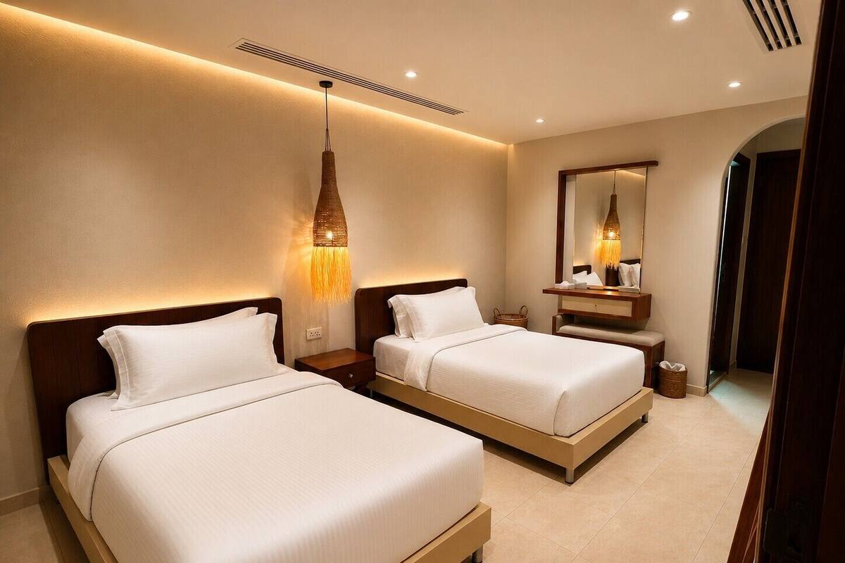 Habitación de hotel con dos camas, una mesita de noche, una lámpara, un espejo y una puerta.