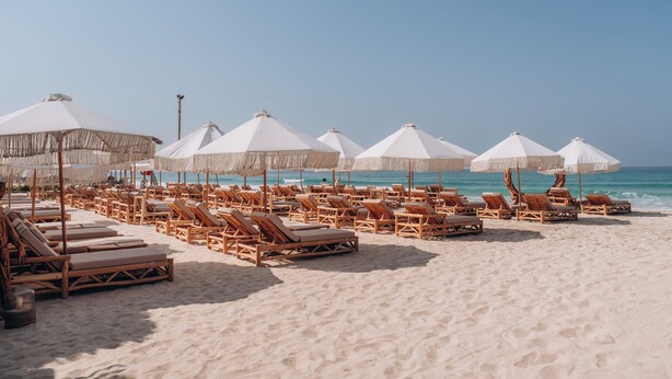 A beach with rows of wooden lounge chairs and white umbrellas. - Umm Al Quwain Beach Hotel (Umm al Quwain)