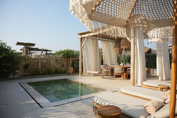 A poolside area with a seating arrangement, a pergola, and a covered seating area.