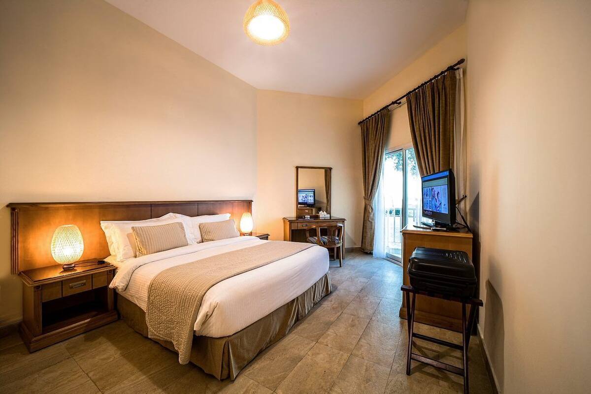 Habitación de hotel con una cama grande, un escritorio con computadora, televisión y lámpara.