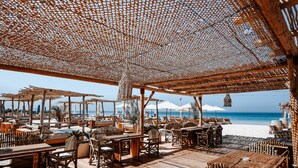 An outdoor seating area with wooden tables and chairs, umbrellas, and a view of the beach and ocean. - Umm Al Quwain Beach Hotel (Umm al Quwain)