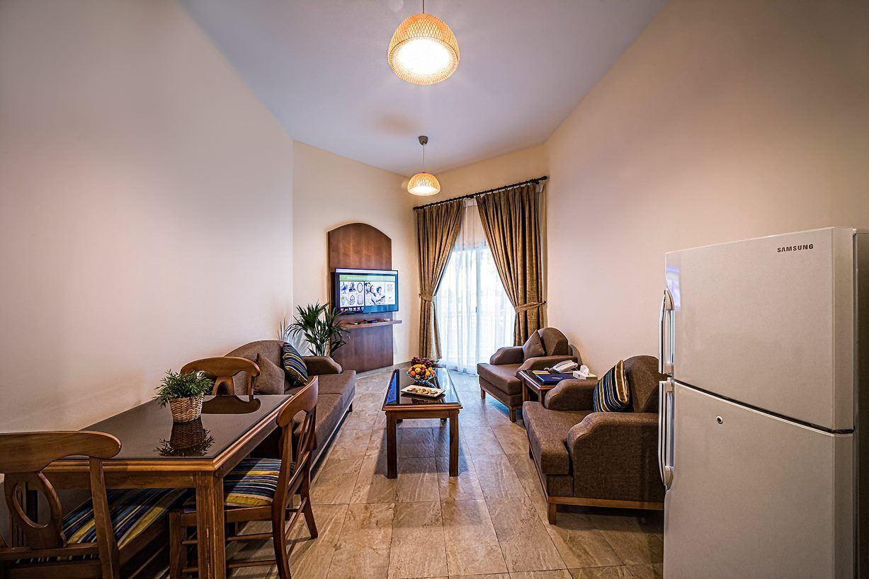 A modern living room with a dining area, a flat-screen TV, a refrigerator, and a cozy seating arrangement.