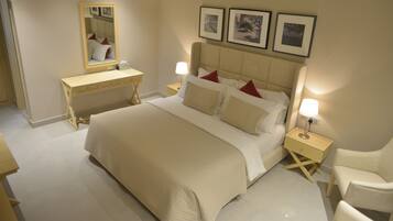 A hotel room with a large bed, bedside tables with lamps, a desk, and a chair. There are framed pictures on the wall above the bed.